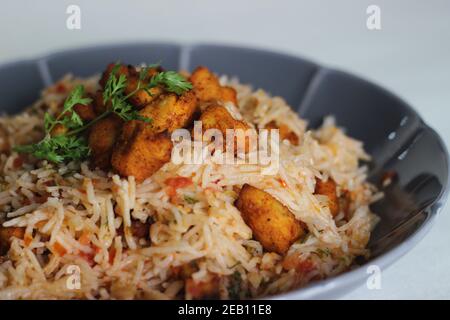 Tomatenreis serviert mit Raita und gebratenen Hähnchenbissen ohne Knochen. Aufnahme auf weißem Hintergrund. Serviert auf einer grauen Schüssel Stockfoto