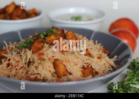 Tomatenreis serviert mit Raita und gebratenen Hähnchenbissen ohne Knochen. Aufnahme auf weißem Hintergrund. Serviert auf einer grauen Schüssel Stockfoto