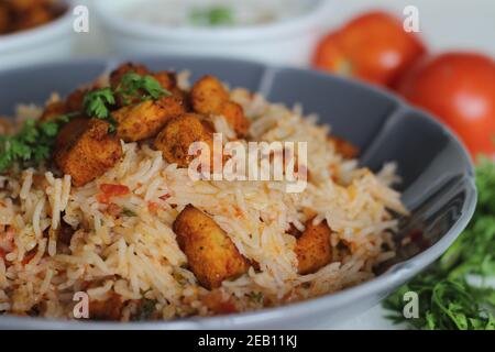 Tomatenreis serviert mit Raita und gebratenen Hähnchenbissen ohne Knochen. Aufnahme auf weißem Hintergrund. Serviert auf einer grauen Schüssel Stockfoto