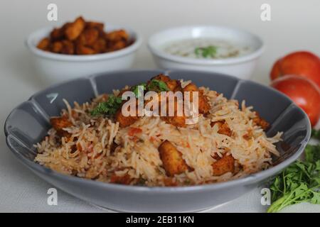 Tomatenreis serviert mit Raita und gebratenen Hähnchenbissen ohne Knochen. Aufnahme auf weißem Hintergrund. Serviert auf einer grauen Schüssel Stockfoto