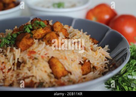 Tomatenreis serviert mit Raita und gebratenen Hähnchenbissen ohne Knochen. Aufnahme auf weißem Hintergrund. Serviert auf einer grauen Schüssel Stockfoto