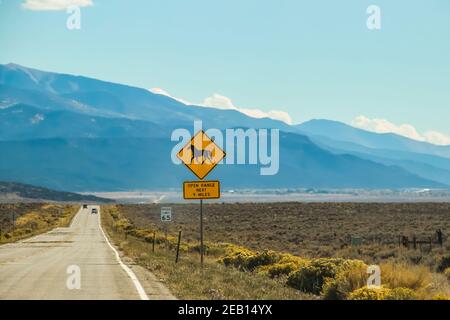 Ein Hitzeschimmern auf der Straße und Autos in der Hohe Wüste mit Bergen in der Ferne und ein Zeichen Mit einem Pferd, das Open Range sagt Stockfoto