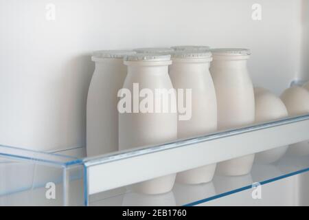 Weiße Flaschen Joghurt auf dem Regal des offenen leeren Kühlschranks. Fermentiertes Lebensmittelkonzept. Stockfoto