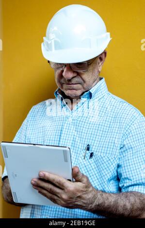 Weißer Mann mit einem weißen Ingenieur-Helm, der ein Tablet hält Stockfoto