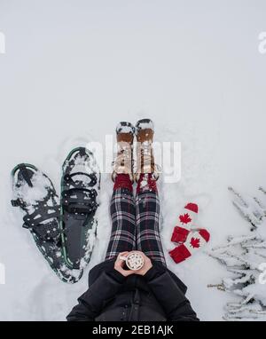 Draufsicht Frau sitzt im Schnee mit Schneeschuhen, Fäustlingen, heißer Schokolade. Stockfoto