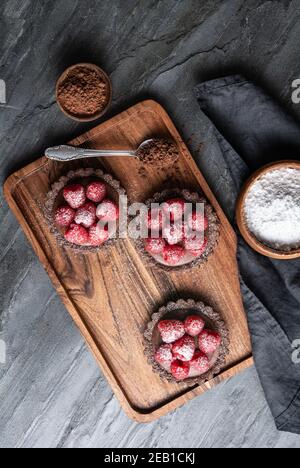 Kakaokrusttörtchen gefüllt mit dunkler Schokoladenmousse aus Schlagsahne und Himbeerpüree, gekrönt mit frischen Beeren, bestreut mit Puderpulver Stockfoto