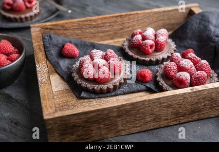 Kakaokrusttörtchen gefüllt mit dunkler Schokoladenmousse aus Schlagsahne und Himbeerpüree, gekrönt mit frischen Beeren, bestreut mit Puderpulver Stockfoto