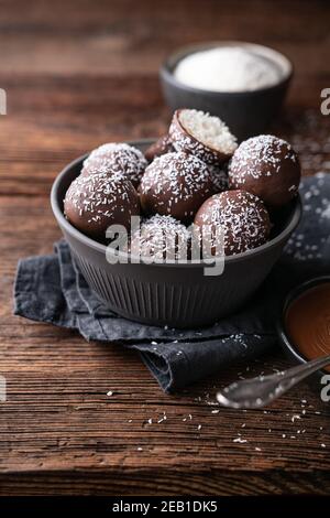 Kein Backen köstliche Süßigkeiten, süße Kokosnusskugeln in Schokolade getaucht auf rustikalem Holzhintergrund Stockfoto