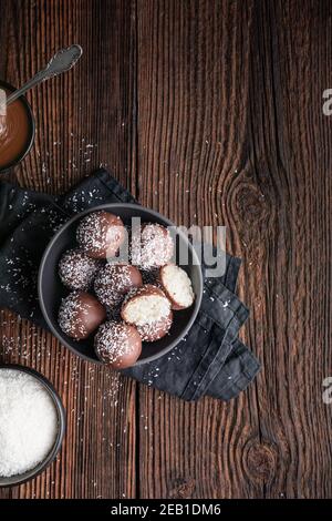 Keine Backen köstliche Süßigkeiten, süße Kokosnusskugeln in Schokolade getaucht auf rustikalem Holzhintergrund mit Kopierraum Stockfoto