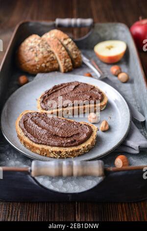 Gesundes Frühstück, Scheiben Vollkornbrot mit Apfelaufstrich aus Kakaopulver, geröstete gemahlene Haselnüsse und dunkle Schokolade auf rustikalem Holz Stockfoto