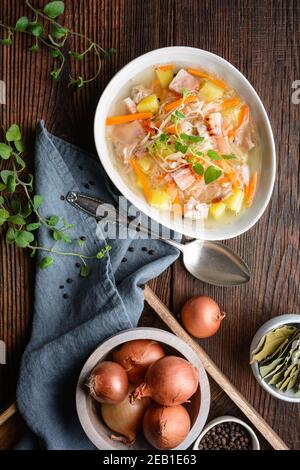 Kapusniak, klassische polnische Suppe aus Sauerkraut, Schweinebrippen, geräuchertem Speck, Kartoffeln, Karotten und anderem Gemüse in tiefer Keramikplatte auf rustikalem Holz Stockfoto