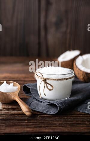 Superfood kaltgepresstes Bio-Kokosöl in einem Glas, mit frischer Nuss auf rustikalem Holzhintergrund mit Kopierraum dekoriert Stockfoto