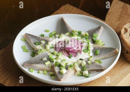 Heringsfilets mit Sahnesauce mit Gurken, roter Zwiebel und Gewürzen auf Schneidebrett Stockfoto