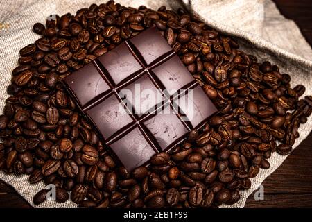 Kaffee in einer Glastasse auf einem Holzhintergrund. Kaffeebohnen und Schokoladenstücke. Stockfoto