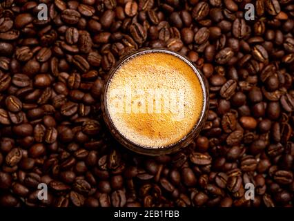 Kaffee in einer Glastasse auf einem Holzhintergrund. Kaffeebohnen und Schokoladenstücke. Stockfoto