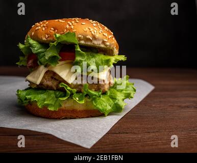 Burger mit Hähnchenschnitzel, Käse, Tomaten und Kräutern. Stockfoto