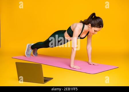 Ganzkörperfoto der sportlich motivierten jungen Dame stehen auf Arme Plank tragen grünen Anzug isoliert gelbe Farbe Hintergrund Stockfoto