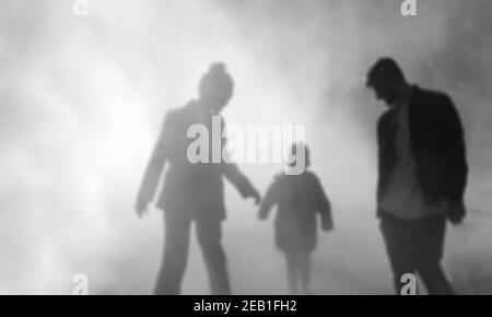 Verschwommenes Foto von Silhouetten von Paar mit Kind im Nebel. Beziehungen im abstrakten Hintergrund der Familie. Schwarzweiß-Foto Stockfoto