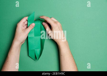 Entstehungsprozess eines Origami Klee: Junge Hände Falten ein grünes Stück Papier, auf einem grünen Hintergrund. Bild mit Kopierbereich. Stockfoto