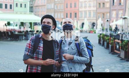 Mann und Frau Touristen in Schutzmasken und mit Taschen mit Smartphone. Sie suchen nach interessanten Sehenswürdigkeiten. Stockfoto