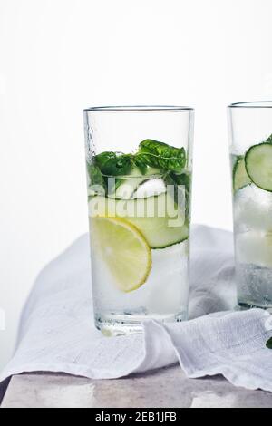 Sommerlicher erfrischender Drink, Tonic mit Zitrone, Gurke und Basilikumblättern in einem hohen Glas auf hellem Hintergrund. Stockfoto