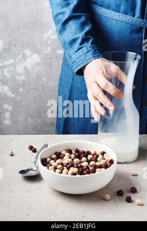 Weibliche Hände gießen Milch in eine Schüssel mit Frühstückscerealien. Stockfoto