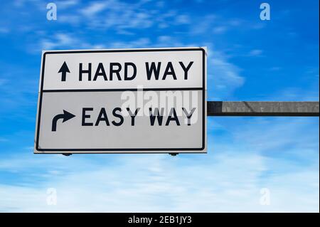 Straßenschild mit Worten Hard Way und Easy Way. Weiße zwei Straßenschilder mit Pfeil auf Metallmast. Richtungsstraße, Wegzeichen Kreuzung, zwei Pfeil. Stockfoto