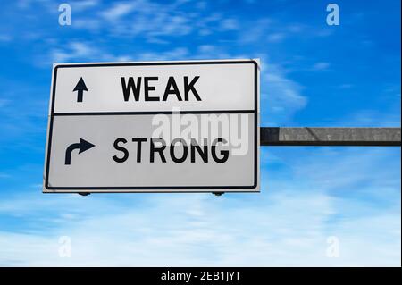 Straßenschild mit Worten schwach und stark. Weiße zwei Straßenschilder mit Pfeil auf Metallmast. Richtungsstraße, Wegzeichen Kreuzung, zwei Pfeil. Blauer Himmel Stockfoto