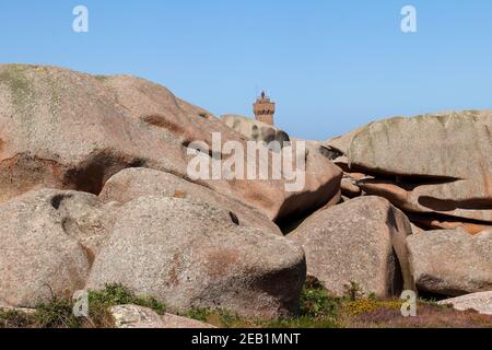 Felsbrocken an der Pink Granite Coast - Cote de Granit Rose - im Hintergrund die Spitze des Mittelwerts Ruz Lighthouse Stockfoto