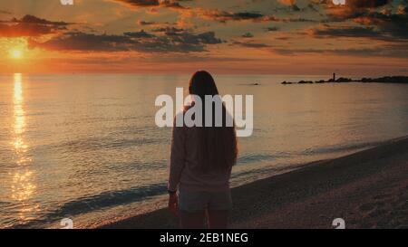 Frau mit ausgestreckten Armen genießen die Schönheit des Sonnenuntergangs auf dem Meer. Kranschuss. Stockfoto
