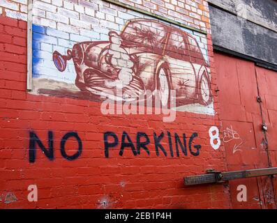 Bemalte Wand eines alten zertrümmerten Mini und ein Schild mit der Aufschrift No Parking neben dem Eingang eines alten Gebäudes. Stockfoto