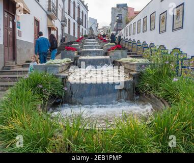 Firgas, Gran Canaria, Kanarische Inseln, Spanien 13. Dezember 2020: Blick auf die Straße Paseo de Gran Canaria mit Wasserfall Brunnen, Blumen und Keramik Stockfoto