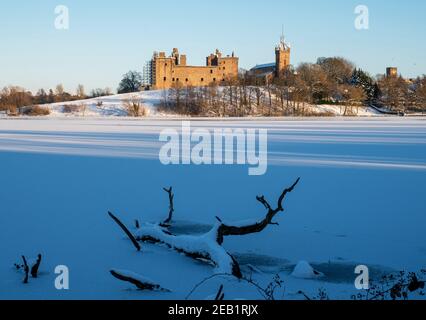 Winterszene Schottland: Die Sonne geht auf einem gefrorenen Linlithgow Loch und Linlithgow Palace unter. Stockfoto