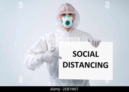 Gesundheitsarbeiter in Schutzanzug und medizinische Maske Punkte auf Text „SOZIALE DISTANZIERUNG“ Stockfoto