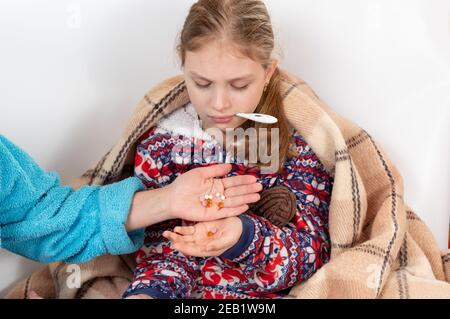 Mama gibt dem Kind viele Pillen. Mama behandelt das Kind. Ein Kind mit einem Thermometer im Mund. Behandlung zu Hause. Stockfoto