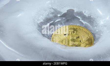 Nahaufnahme der Goldmünze der Kryptowährung Bitcoin fror in Eis. Stockfoto