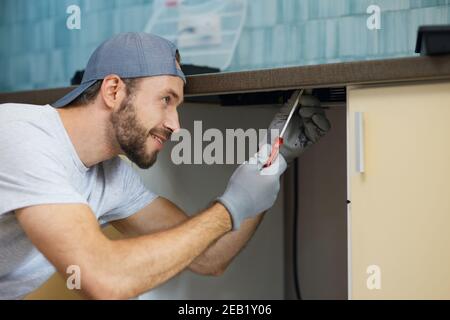 Richtig machen. Portrait des jungen Reparaturmannes, professionelle Klempner suchen konzentriert, während die Befestigung Spülrohr in der Küche drinnen Stockfoto