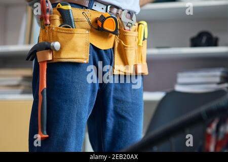 Nahaufnahme des Reparaturwerkzeuges, der einen Werkzeuggürtel trägt, sich auf die Arbeit vorbereitet, im Haus steht Stockfoto