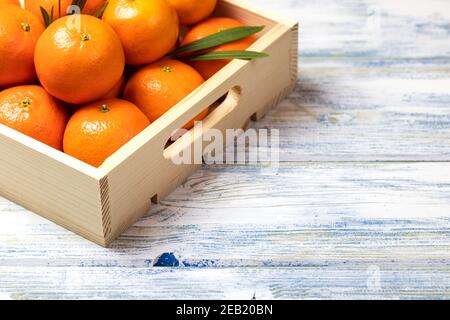 Orangefarbene Früchte in Kiste auf weißem Holztisch. Tropische Zitrusfrüchte. Speicherplatz kopieren Stockfoto