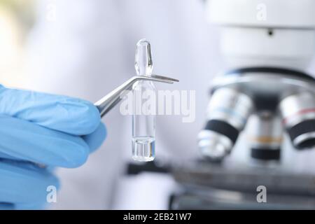 Hand in Handschuh hält Fläschchen mit Impfstoff vor dem Hintergrund von Mikroskop Stockfoto