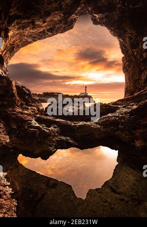 Leuchtturm von Portocolom, Mallorca, von innen gesehen eine Höhle bei Sonnenaufgang mit einer Pfütze im Vordergrund, die den Himmel reflektiert Stockfoto