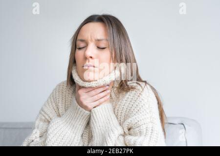 Junge Frau in gemütlichen Pullover berühren schmerzhaften Hals. Halsschmerzen, entzündete Kehle. Coronavirus-Symptom Stockfoto