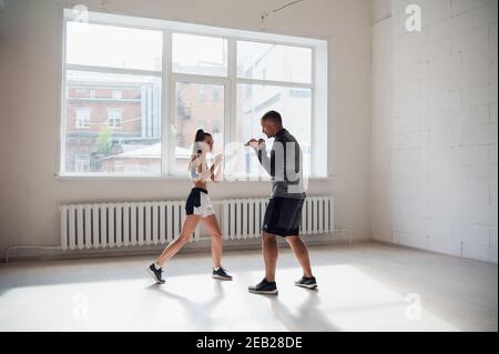 Ein erfahrener Trainer setzt die Technik der Schläge auf ein Junges Mädchen in der Boxhalle Stockfoto