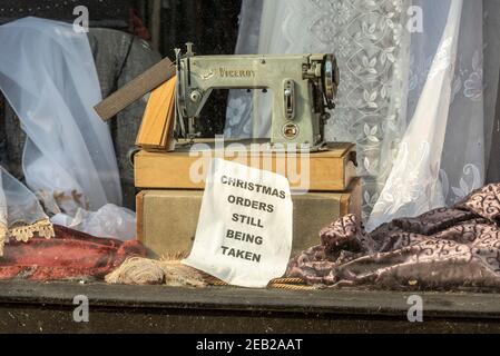 Vintage Viceroy Nähmaschine im Schaufenster, mit Schild, das angibt, dass Weihnachtsaufträge noch angenommen werden. Februar 2021. Geschlossen wegen COVID 19-Sperre Stockfoto