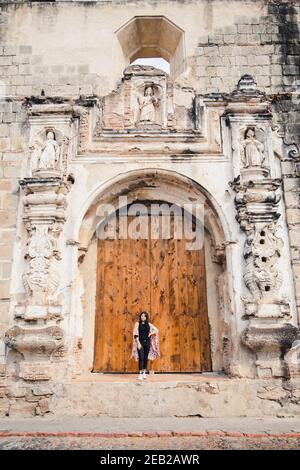 Hispanische Frau, die vor einer alten Kolonialtür steht In einem ehemaligen Kloster in Antigua Guatemala - Barockkirche Ruinen in der Kolonialstadt Stockfoto