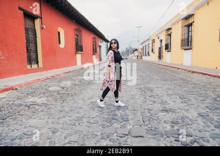 Full Portrait der hispanischen Frau zu Fuß in der Kolonialstadt auf Ein wolkiger Tag - Touristen überqueren die Straße in Antigua Guatemala Stockfoto