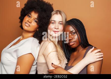 Junge hübsche kaukasische, afro, skandinavische Frau posiert fröhlich zusammen auf braunem Hintergrund, Lifestyle diverse Nationalität Menschen Konzept Stockfoto