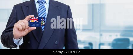 Zugeschnittenes Bild von Geschäftsmann hält Kunststoff-Kreditkarte mit bedruckter Flagge von Süd-Georgien und den Südlichen Sandwich-Inseln. Hintergrund unscharf. Stockfoto