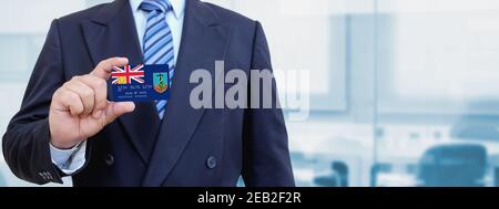 Zugeschnittenes Bild eines Geschäftsmannes, der eine Plastikkreditkarte mit bedruckter Flagge von Montserrat hält. Hintergrund unscharf. Stockfoto