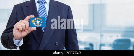 Zugeschnittenes Bild eines Geschäftsmannes, der eine Plastikkarte mit bedruckter Flagge der Nördlichen Marianen hält. Hintergrund unscharf. Stockfoto